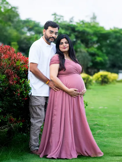 A lovely couple's portrait amidst vibrant red and green foliage. The mom-to-be is wearing a beautiful dusty rose gown from our client wardrobe.