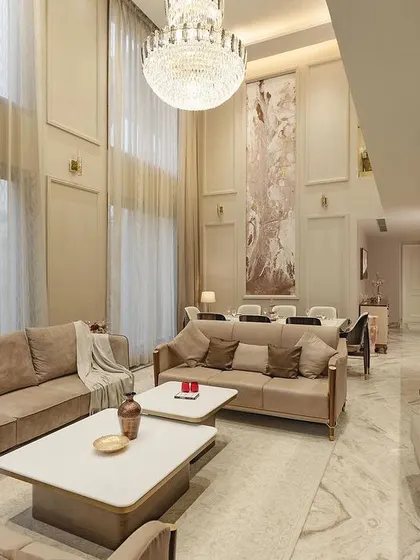 This double-height drawing room in our neoclassical project exudes opulence. The towering walls with classic molding, a grand crystal chandelier, and plush, neutral-toned furniture create a space that is both majestic and inviting.