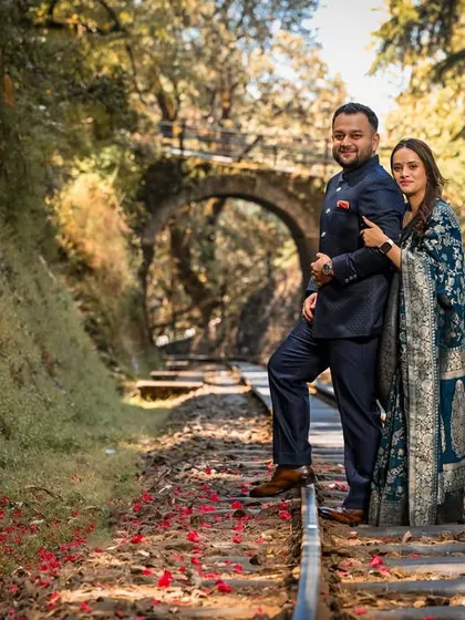 Posing on the historic railway tracks near a stone bridge, this couple's formal attire contrasts beautifully with the rustic, natural surroundings of the Shimla hills.