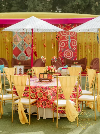Guest seating featuring tables draped in vibrant phulkari-inspired linen. The backdrop includes traditional printed panels, creating a cohesive and colorful look.