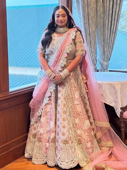 A full-length shot of the bride by a window, showcasing her stunning pastel lehenga.