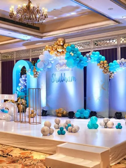 A cool and stylish 15th birthday party setup. I used a blue, white, and gold color palette with modern arched backdrops, balloon garlands, and light-up marquee numbers for a fun and elegant stage.
