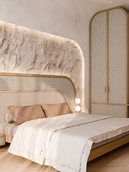 We create bedrooms that feel like a homecoming to calm. This space uses a palette of natural textures, including a raw stone feature wall with soft backlighting and a headboard blending cane and fabric, to craft a sanctuary of quiet luxury.