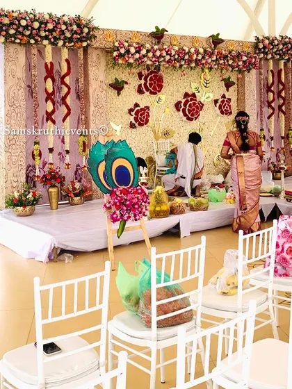 A beautiful outdoor naming ceremony with a backdrop of white flowers and golden rose motifs. The setup includes white chairs for guests, creating an elegant and serene atmosphere.