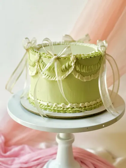 An elegant vintage-style cake in a lovely sage green. The delicate white swag piping and sheer ribbons create a light and airy design.