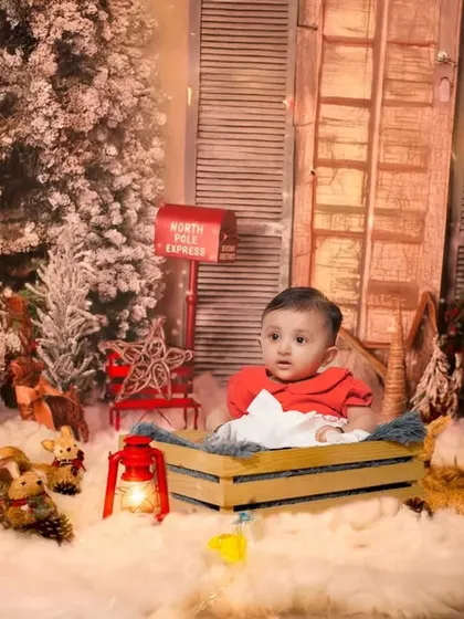 A festive Christmas-themed baby shoot. The set is complete with faux snow, decorated trees, and a cozy wooden crate, creating a perfect holiday memory.