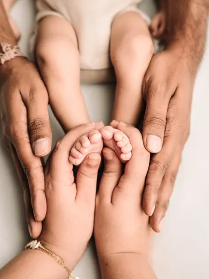 Both parents' hands come together to hold their baby's feet, creating a beautiful heart shape.