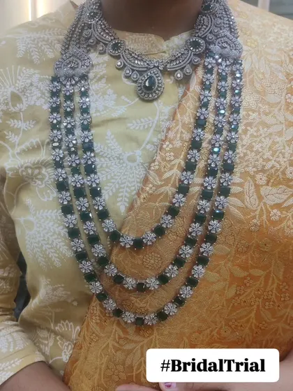 A client trying on a Victorian-style necklace with emerald green stones during her bridal trial. This process helps ensure the jewellery perfectly complements the outfit and the bride's personal style.