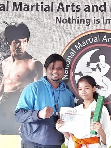 A young girl proudly holds her new orange belt and certificate.