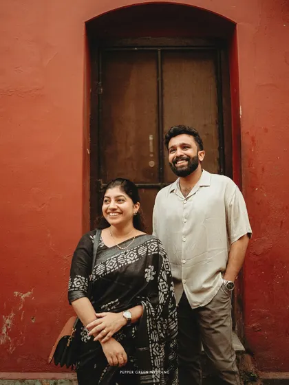 Anna and Freddy posing against a vibrant red wall in Fort Kochi. The bold color creates a striking contrast with their outfits and adds a modern touch to the vintage setting.