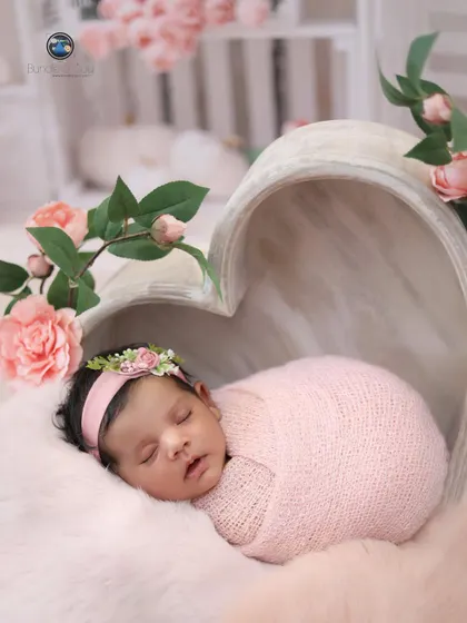 Pretty in pink. This baby girl is nestled in a heart-shaped bowl, surrounded by soft pink fur and delicate pink roses for a romantic and classic floral portrait.