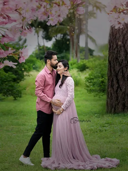 A romantic couple's portrait under a tree with pink blossoms. The mother-to-be's pink lace gown is perfect for this dreamy setting.