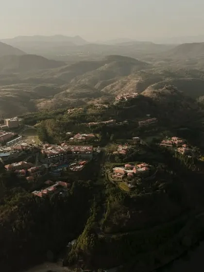 An even wider establishing shot of the ITC property in Udaipur, showing the resort complex in the context of the surrounding hills and nearby lake. This type of large scale aerial photography is essential for showcasing the location's exclusivity and scale.