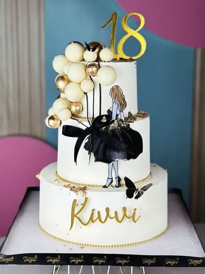 Understated luxury. This minimalist white, black, and golden cake for an 18th birthday is a masterpiece of simplicity and elegance, featuring a chic silhouette and balloon accents.