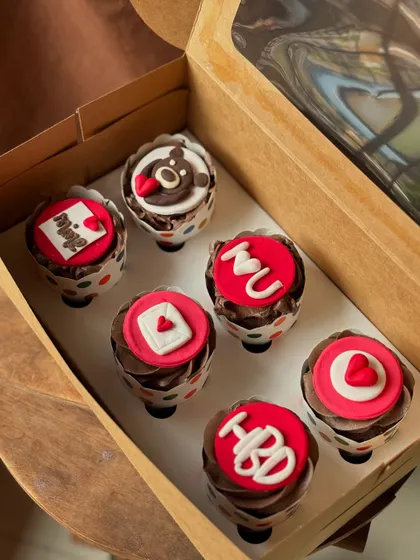 A closer look at the custom love-themed cupcakes. The fondant toppers include messages like "I heart U", "Mine", and a cute teddy bear.