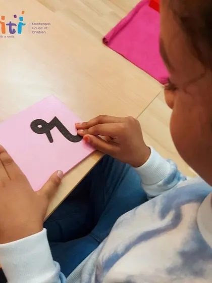 A child gently traces a sandpaper vowel, her focus entirely on the task. This activity builds concentration as well as pre-writing skills.