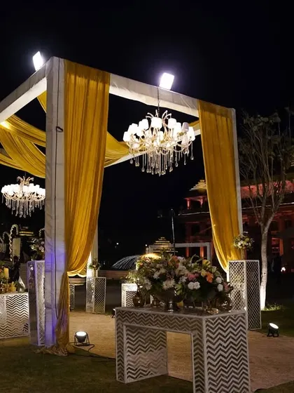 The entrance structure for the 'Golden Grandeur' theme, featuring a modern white frame with golden drapes and a hanging chandelier, setting a tone of contemporary luxury.