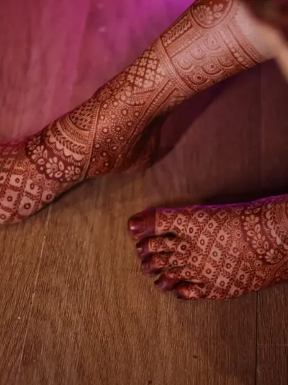 A close-up of the bride's feet, showing the rich stain of the intricate leg mehendi. The pattern is dense and covers the entire foot.