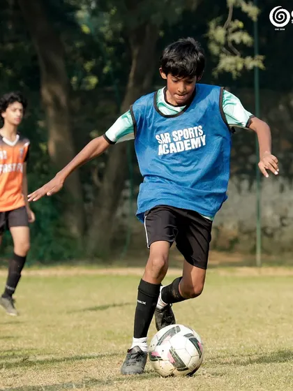 A player in a blue bib dribbles the ball during a training game.