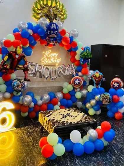 An exciting Avengers-themed birthday decoration for a 6th birthday. This setup includes character cutouts, a neon sign, and a balloon arch in superhero colors.