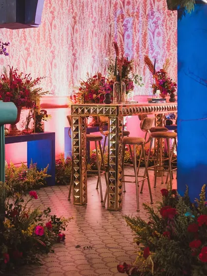 A wider view of the sangeet bar area, showing how the different colored elements and lush florals come together to create a rich, multi-dimensional space.