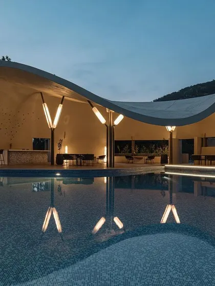 This is the Aqua Pool & Spa, a modern cave-like structure designed to celebrate the surrounding hills. The evening view highlights the custom lighting which reflects in the water, creating a tranquil and immersive atmosphere that blends architecture with the natural landscape.