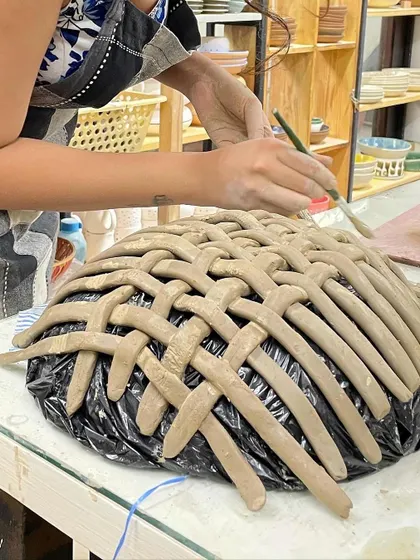 A student works on a large, woven bowl, carefully placing each strip of clay. This is an advanced hand-building project from our 10-day course.