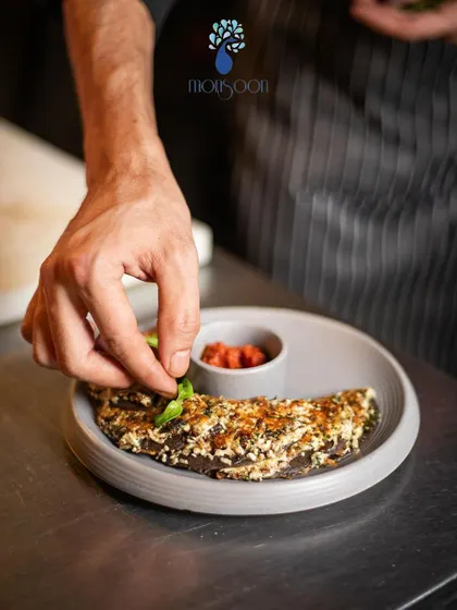 A chef at Monsoon carefully plating a dish. This image emphasizes the craftsmanship and attention to detail that goes into every meal served here.