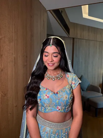 A modern and fresh half-updo with long, flowing waves. The look is completed with a delicate floral hairpiece, perfect for a daytime wedding or Mehendi.