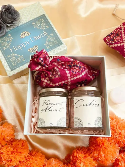An open view of the light blue gift box, containing two jars of almonds and cookies and a traditional potli.