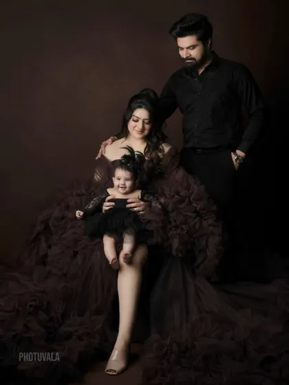 A dramatic and loving family portrait. The dark, moody tones and the mother's beautiful ruffled gown create a stunning, high-fashion look for this family of three.