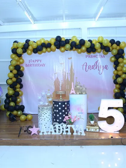 Another 'Sofia the First' party setup, this time with a black and yellow balloon arch, a large light-up number '5', and character cutouts for a princess-themed celebration.