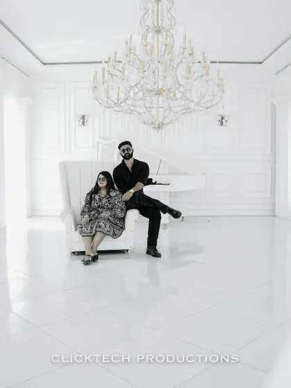 A minimalist and high-contrast shot of a couple in a stark white room with a grand piano and chandelier, creating a modern, artistic look.