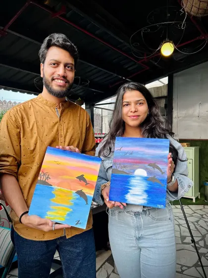 A couple proudly displaying their finished dolphin sunset paintings. It's so lovely to see partners create their own unique versions of the same theme.