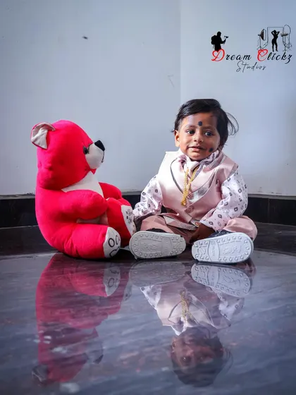 A cute indoor baby portrait with a prop. The baby is sitting next to a bright pink teddy bear, and their reflection on the glossy floor adds a creative touch to the shot.