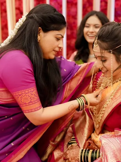 Final touches from a loved one. The bride's makeup is set, providing a perfect canvas for her traditional Maharashtrian jewelry.
