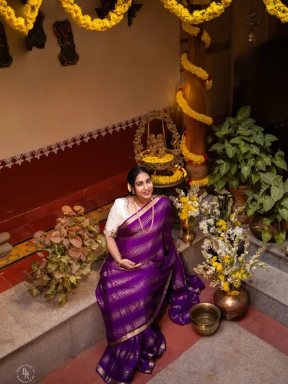 A wide shot showing the beautiful traditional setup for a maternity shoot, with the expectant mother seated gracefully amidst flowers and plants.
