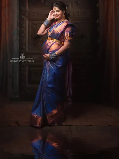 A fine art maternity photoshoot featuring a stunning blue and gold silk saree, capturing the regal elegance of motherhood.