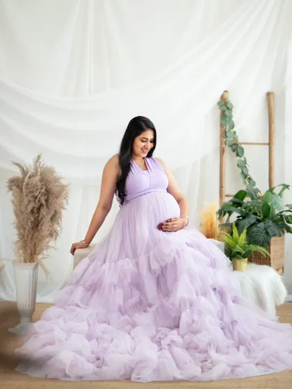 A beautiful solo portrait of a mom-to-be in a lavender ruffled gown, set against our lush and green boho studio setup.