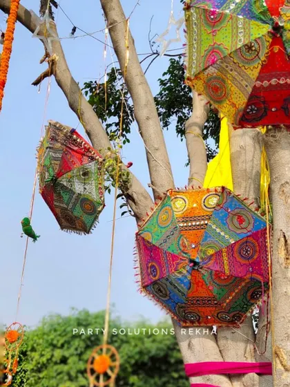Hanging decorative umbrellas from tree branches is a simple yet effective way to add a touch of Rajasthani charm and color to an outdoor Mehendi or Haldi event.