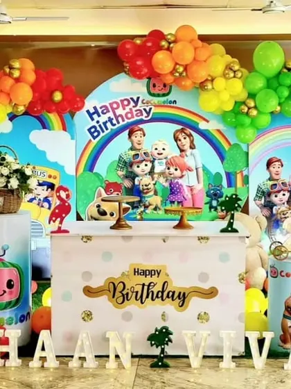 A vibrant and colorful Cocomelon themed birthday party. The setup is filled with characters from the show, a rainbow balloon arch, and custom name and age displays for a cheerful celebration.
