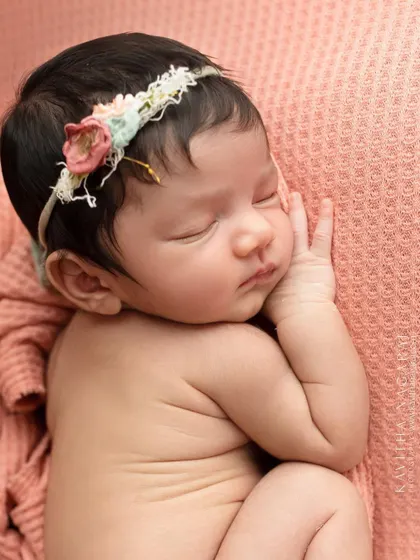A newborn girl in a side-lying pose, wearing a floral headband. This classic pose is perfect for showcasing the baby's delicate profile and curled-up form.