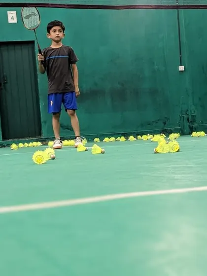 A junior player stands ready with his racket, surrounded by the tools of his training.