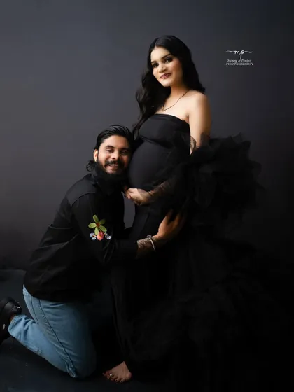 A joyful and loving pose. The father-to-be kneels to hug his partner's baby bump, both sharing a beautiful smile.