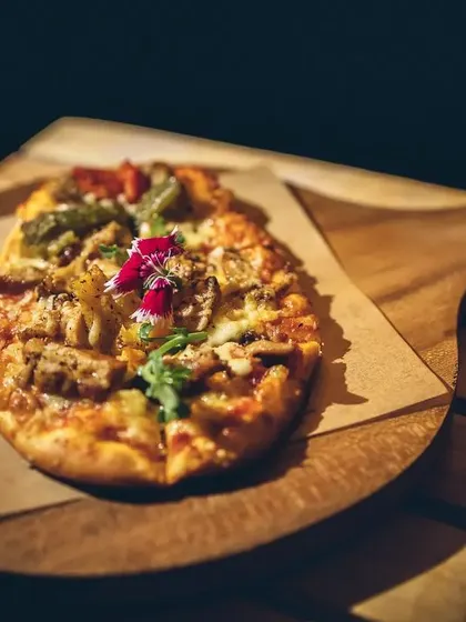 A delicious-looking flatbread pizza on a wooden board, under dramatic lighting.