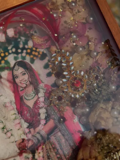 A close-up of a teakwood frame, preserving a bride's beautiful photo along with her wedding jewelry. You can see the intricate details of the nath and other ornaments, saved forever as part of her story.