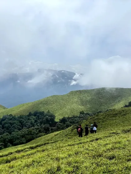 Trekkers on a ridge, with clouds rolling in over the green hills.