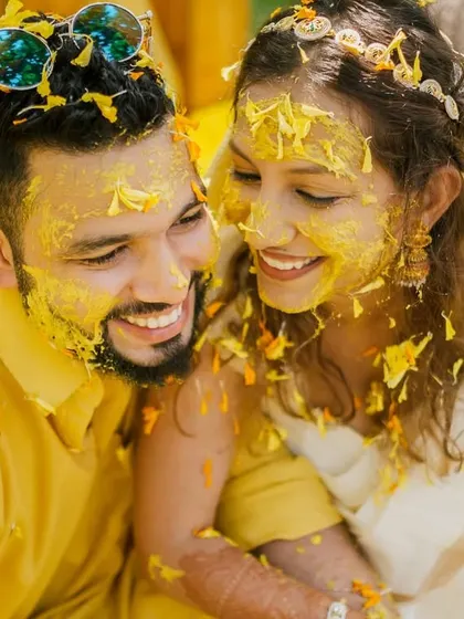 A sweet, candid moment of the couple, their faces covered in turmeric and marigold petals, smiling at each other during their Goa haldi.