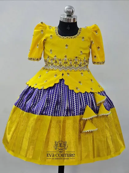 A yellow peplum top paired with a striped blue and white skirt. The entire Kanchi pattu lehenga is tied together with a matching yellow border and tassels.