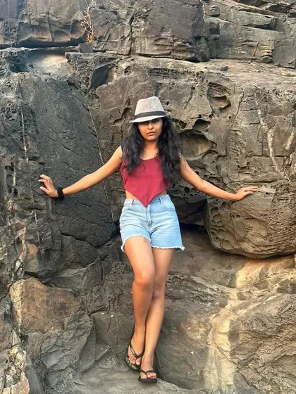 A full-length shot against a rocky cliff in Goa. This photo shows a complete travel outfit and a confident pose that suits adventure and fashion brands.